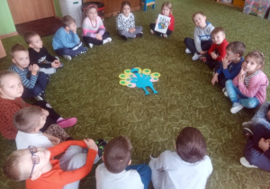 Dzieci z grupy 2 siedzą w kole i prezentują wykonanego pawia.