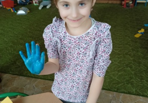 Dziewczynka z grupy 2 z pomalowaną na niebiesko w farbie dłonią.